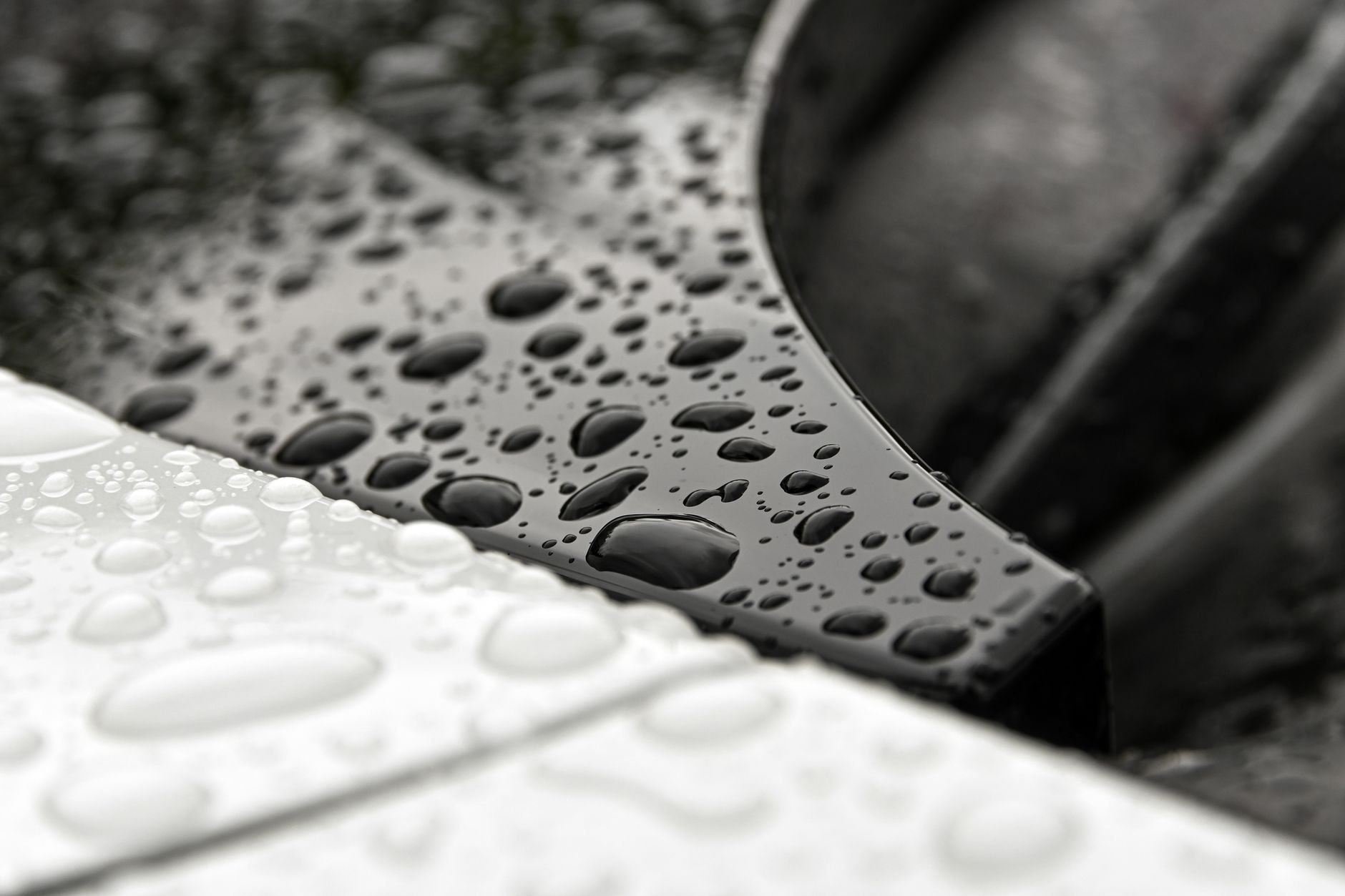 Macro shot of water droplets on black and white metallic car surface.